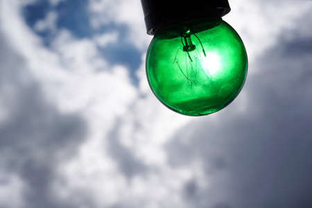 Green Edison light bulb isolated on beautiful cloudy skyの素材