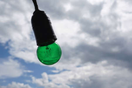 Green Edison light bulb isolated on beautiful cloudy skyの素材