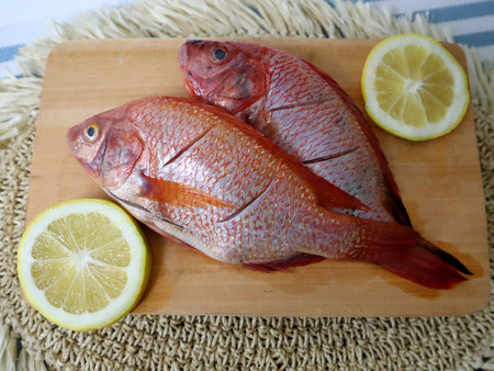 Red tilapia fish on cutting board with lemon and straw.