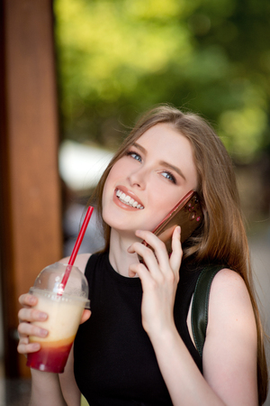 Young beautiful stylishly dressed girl is walking along the streets of the city, drinking juice, coffee, talking on mobile phoneの写真素材