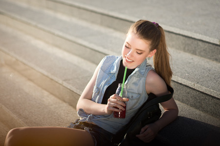 A beautiful young stylishly dressed girl walks in the city, drinks juice or a cocktail,の写真素材
