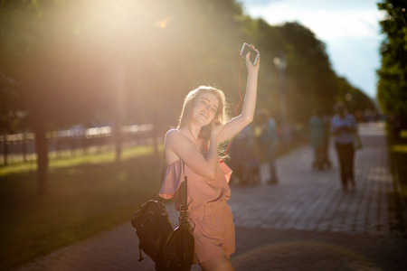 Young beautiful stylishly dressed girl with beautiful hair is walking along the streets of the city at sunset, in sunny rays and listen to musicの写真素材