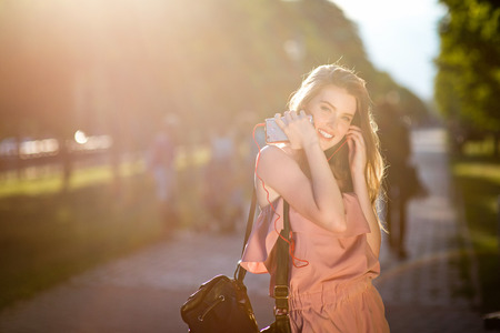 Young beautiful stylishly dressed girl with beautiful hair is walking along the streets of the city at sunset, in sunny rays and listen to musicの写真素材