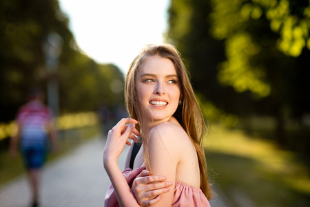 Young beautiful stylishly dressed girl with beautiful hair is walking along the streets of the city at sunset, in sunny raysの写真素材
