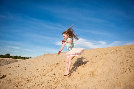 Little active girl  walking, running, jumping, having fun along the sand on the beach against the background blue sky in summer vacationの写真素材