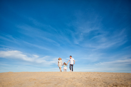 Happy beautiful laughing family running along the sand on the beach against the background blue sky in summer vacationの写真素材