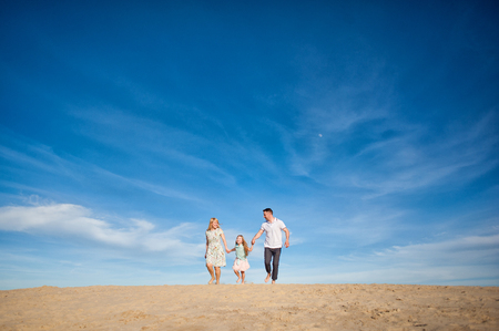 Happy beautiful laughing family running along the sand on the beach against the background blue sky in summer vacationの写真素材