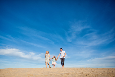 Happy beautiful laughing family running along the sand on the beach against the background blue sky in summer vacationの写真素材