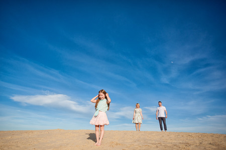 Beautiful happy family walking, running, jumping, having fun along the sand on the beach against the background blue sky in summer vacationの写真素材