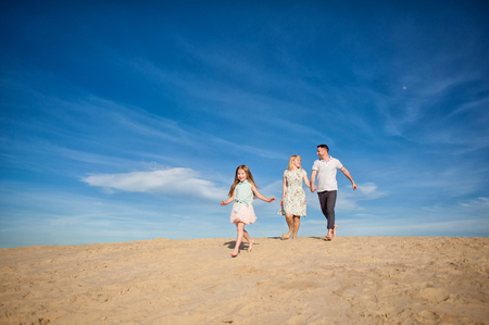 Happy beautiful laughing family running along the sand on the beach against the background blue sky in summer vacationの写真素材