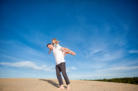 Dad and little girl daughter playing on the beach, fly, run, laugh at the blue sky backgroundの写真素材