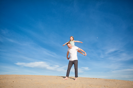 Dad and little girl daughter playing on the beach, fly, run, laugh at the blue sky backgroundの写真素材