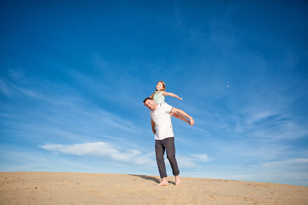 Dad and little girl daughter playing on the beach, fly, run, laugh at the blue sky backgroundの写真素材