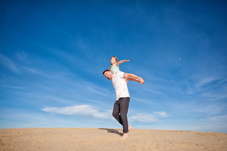 Dad and little girl daughter playing on the beach, fly, run, laugh at the blue sky backgroundの写真素材