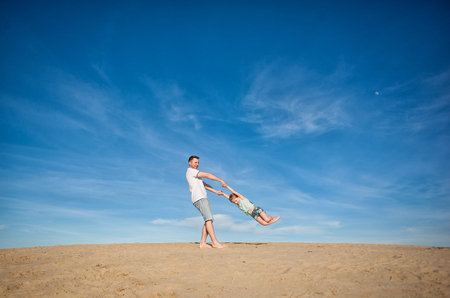 Dad and little girl daughter playing on the beach, fly, run, laugh at the blue sky backgroundの写真素材