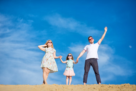 Beautiful happy family walking, running, jumping, having fun along the sand on the beach against the background blue sky in summer vacationの写真素材