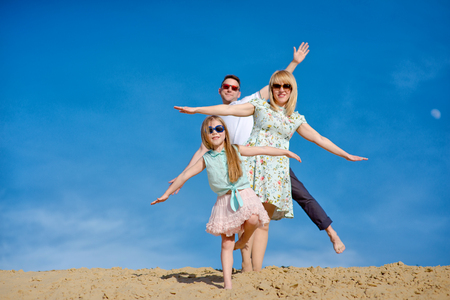 Beautiful happy family walking, running, jumping, having fun along the sand on the beach against the background blue sky in summer vacationの写真素材