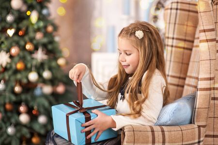 Girl, daughter, smiling, glad opens and receives gifts on Christmas Eve or New Year near Christmas treeの写真素材