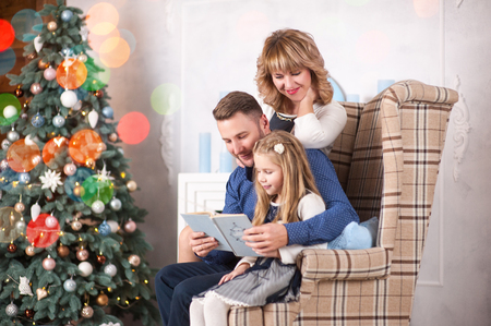 Family of mother, father and little child daughter near Christmas tree with presents, decorations and New Year or Christmasの写真素材