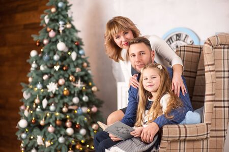 Family of mother, father and little child daughter near Christmas tree with presents, decorations and New Year or Christmasの写真素材