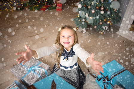 Girl, daughter, smiling, glad opens and 
receives gifts on Christmas Eve or New Year near Christmas treeの写真素材