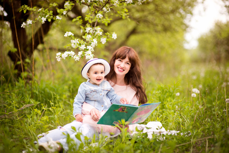 Mother reading a book with tales  to little daughter outdoors in the garden or the parkの写真素材