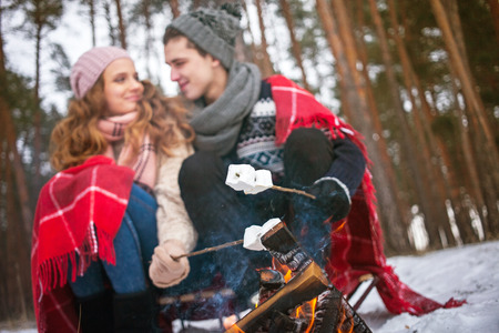 Couple embracing sitting near the fire in the winter, it is snowing, lit sparklers, roast...