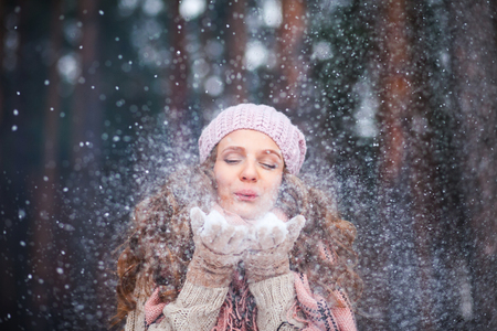 Girl wearing warm winter clothes and hat play ,smile and blowing snow in the winter forestの写真素材