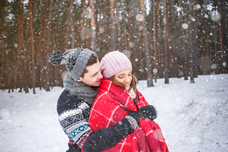 The guy embraces the girl and covers it with a warm blanket in the winter forest, couple of loversの写真素材