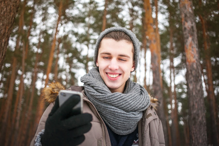 The young man in winter clothes holding a mobile phone and looking at its screenの写真素材