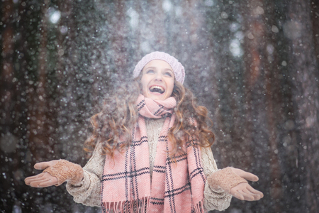 Beautiful girl with long hair man in love catching snowflakes and laughing in winter forest during a snowfall, photos with toningの写真素材