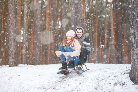 Young couple in winter forest sledding, laughing during snowfallの写真素材