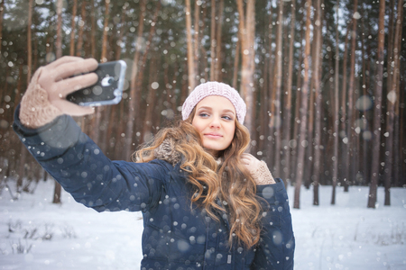 Young woman taking picture with smartphone selfie stick on over winter backgroundの写真素材