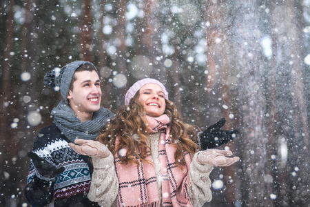 Beautiful girl with long hair man in love catching snowflakes and laughing in winter forest during a snowfallの写真素材