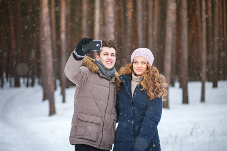 happy couple taking picture with smartphone selfie stick on over winter backgroundの写真素材