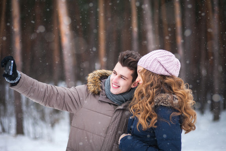 happy couple taking picture with smartphone selfie stick on over winter backgroundの写真素材
