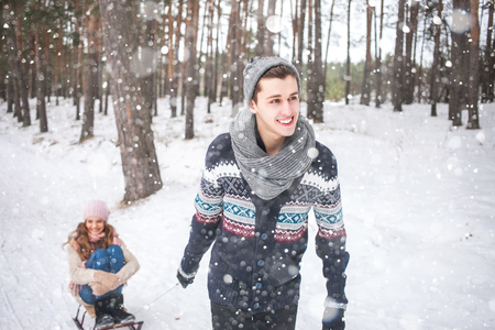 Young couple in winter forest sledding, laughing during snowfallの写真素材