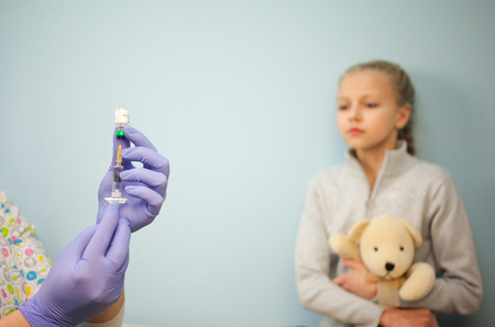 The pediatrician or nurse in a syringe vaccine, a girl in the background with the toy, the child vaccinationの写真素材