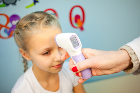 Doctor pediatrician examines girl listening stethoscope, measure the temperature of the body and looks throatの写真素材
