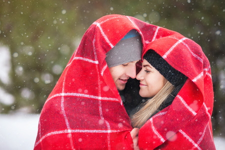 Couple under a red blanket in the winter forest, snow falls, heartの写真素材