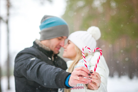 couple is walking in the winter forest and kisses holding candy in the shape of heartの写真素材
