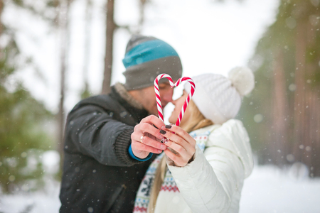 couple is walking in the winter forest and kisses holding candy in the shape of heartの写真素材