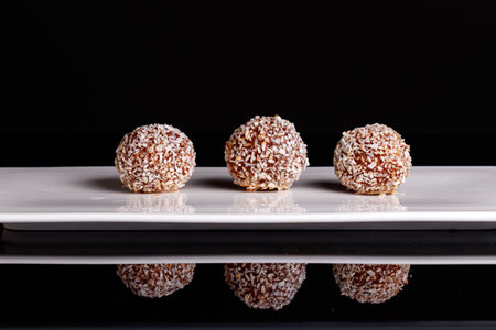 Beautiful sweets with coconut on a white plate on a black background close-up