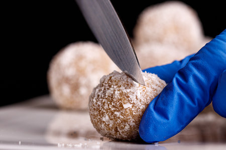Beautiful sweets with coconut are cut with a knife on a white plate on a black background close-upの写真素材