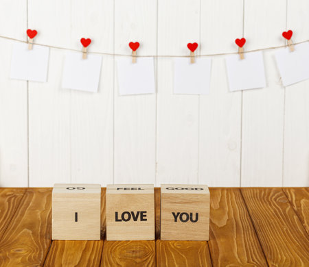 white pieces of paper on clothespins with a heart on a wooden background, a wooden inscription I love you close-upの写真素材