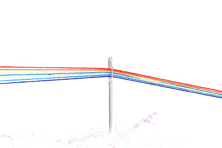 multi-colored threads for sewing in the form of a rainbow pass through an antique needle on a white...