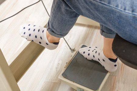 Female feet on the pedal of a sewing machine, motor close-up