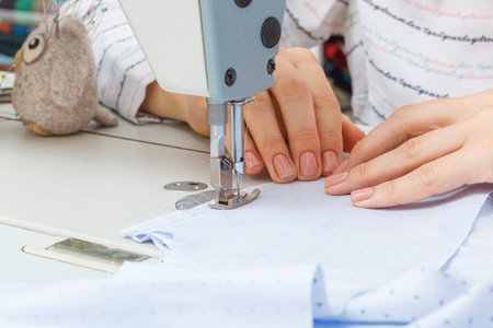Female hands of a master tailor at work, a sewing machine needle close-up