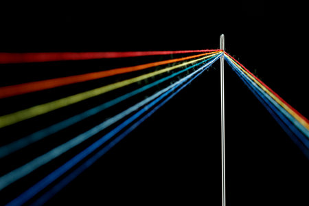 multi-colored threads for sewing in the form of a rainbow pass through an antique needle on a black background close-upの写真素材
