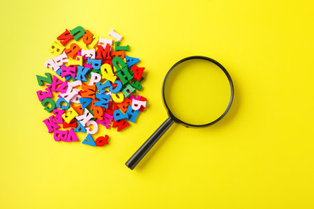 colored letters of the alphabet with a magnifying glass on a yellow background close-upの写真素材